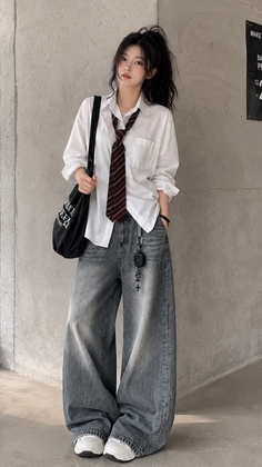 Woman in a white shirt, striped tie, and wide leg jeans standing indoors