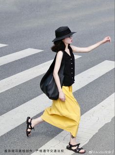 Woman in a black hat and yellow skirt crossing a street