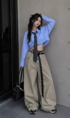 Woman in a cropped blue shirt and wide leg pants with a black tie