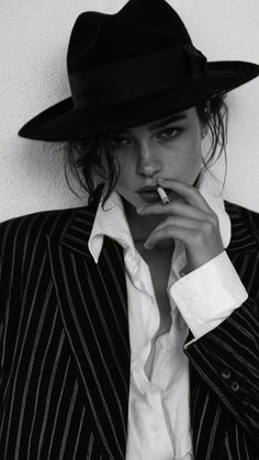 Woman in a fedora hat and pinstripe jacket smoking a cigarette
