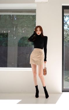 Woman in a black turtleneck and beige mini skirt posing indoors