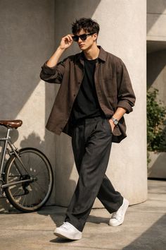 Man in sunglasses, brown shirt, and dark pants walking outdoors next to a bicycle