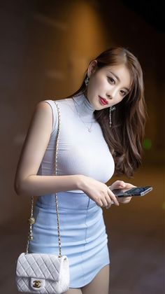 Woman in a light blue top and skirt holding a phone and handbag