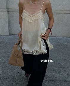 Person in a lace camisole and black pants holding a suede bag outdoors