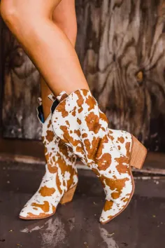 Person wearing brown and white cow print cowboy boots with exposed legs
