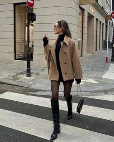 Woman in a camel coat and black dress crossing a city street