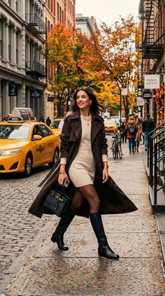 Woman in a long coat and mini dress walking on a city street with autumn leaves