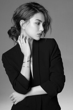 Woman in a suit jacket with a messy bun and jewelry in a black and white studio shot
