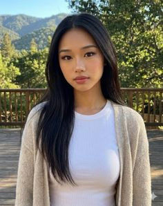 Woman with long black hair wearing a cardigan and white t-shirt on a wooden deck