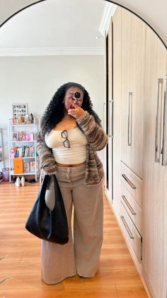 Person with curly hair taking a mirror selfie in a cardigan and wide leg pants