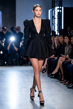 Model in a black dress with puffy sleeves and high heels on a runway