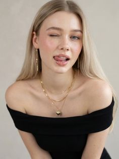 Blonde woman winking with her tongue out, wearing an off-shoulder top and gold jewelry