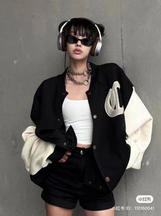 Person in a black and white varsity jacket, headphones, and sunglasses against a gray wall