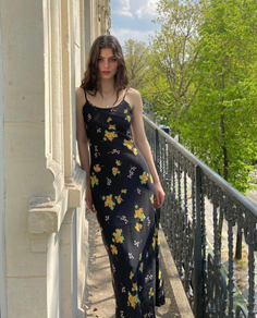 Woman in a black floral dress standing on a balcony outdoors