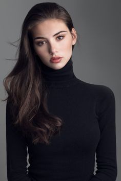 Woman with long dark hair wearing a black turtleneck in a studio setting
