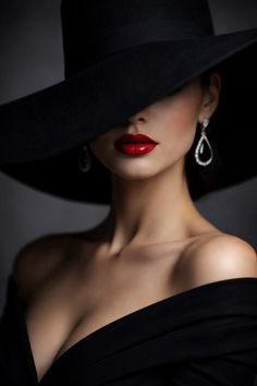 Woman in a black hat and off-shoulder top with red lipstick and diamond earrings