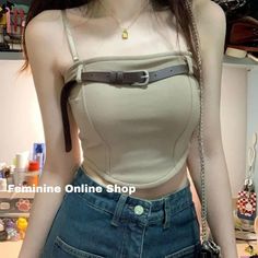 Woman wearing a beige crop top with a belt detail and blue jeans indoors