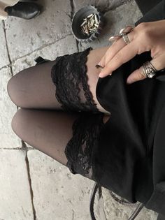 Person wearing black stockings with lace trim and rings, holding a cigarette