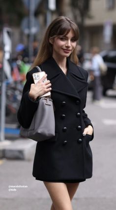Woman in a black coat holding a grey handbag and phone on a street