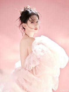 Woman with a messy bun and bare shoulders against a pink background