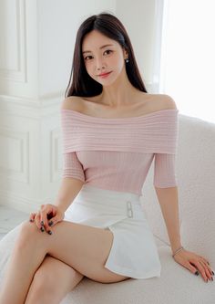 Woman in a pink off-shoulder top and white skirt sitting indoors