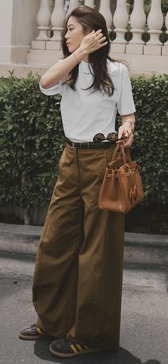 Woman in a white t-shirt and wide leg pants holding a brown handbag outdoors