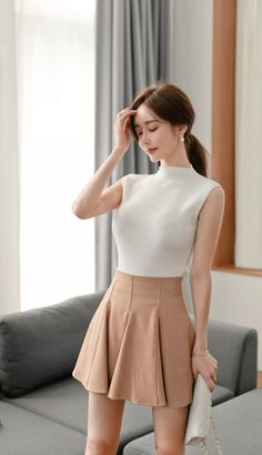 Woman in a white sleeveless top and pleated skirt with a ponytail indoors