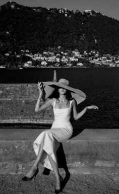 Woman in a wide brim hat and white dress sitting by the water