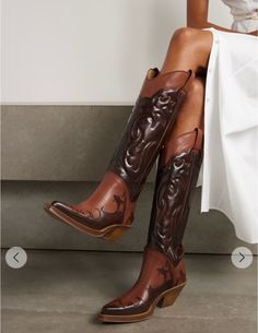 Woman wearing brown cowboy boots and a white dress, sitting indoors