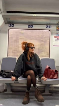 Woman with red hair wearing a hoodie, sunglasses, and headphones on a train