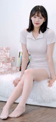Woman with short hair wearing a collared dress, sitting on a white furry rug