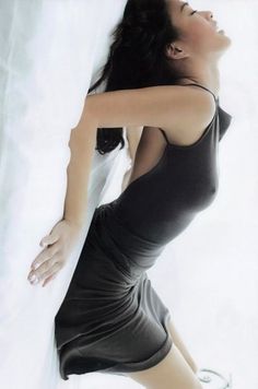 Woman in a dark spaghetti strap dress posing against a white background