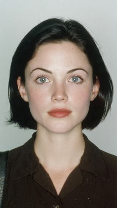 Woman with short black hair and blue eyes wearing a brown collared shirt