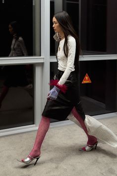 Woman in a leather skirt and pink polka dot tights walking indoors