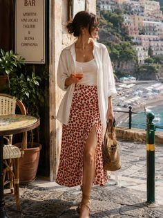 Woman in a floral skirt and white shirt holding a drink in a beach town