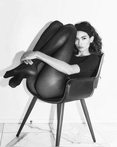 Woman in a black bodysuit and tights sitting in a chair with a provocative pose