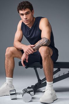 Man with curly hair and tattoos sitting on a gym bench with a dumbbell