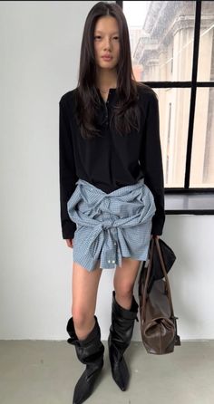Woman with long dark hair wearing a black shirt and plaid skirt with black boots