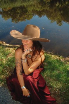 Woman in a cowboy hat and red dress sitting by water with reflections