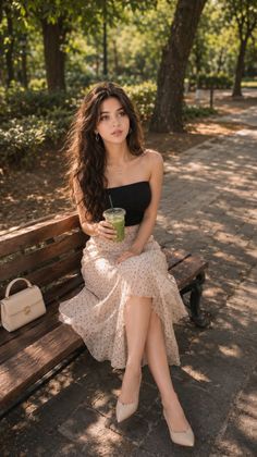 Woman with long hair sitting on a park bench holding a green drink