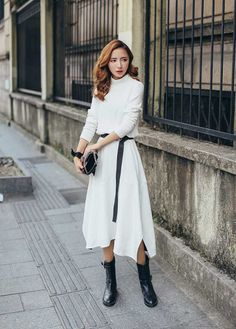 Woman in a white dress with a black belt and boots standing on a street