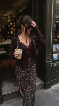 Woman in a cardigan and floral skirt holding an iced coffee on a street