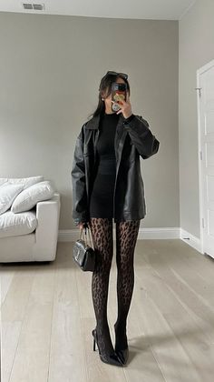 Woman in a black dress, leather jacket, and leopard print tights holding a handbag