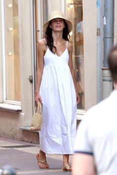 Woman in a white dress and straw hat walking on a street