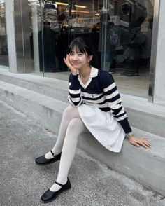 Woman in a striped sweater and white skirt sitting on concrete steps outdoors
