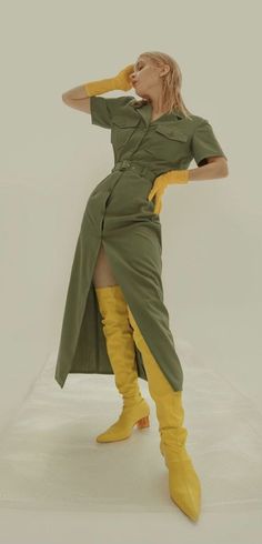 Woman in a khaki dress with yellow gloves and boots posing in a studio