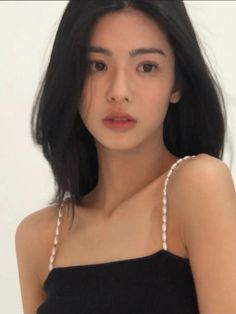 Woman with black hair and a black top with pearl straps