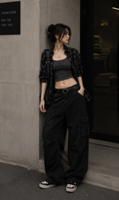 Woman in a plaid shirt and baggy pants leaning against a wall