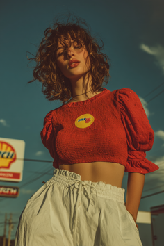 Woman with curly hair in a red crop top and white pants outdoors