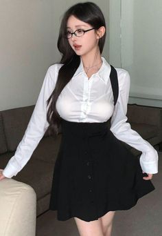 Woman with long dark hair and glasses wearing a white shirt and black dress